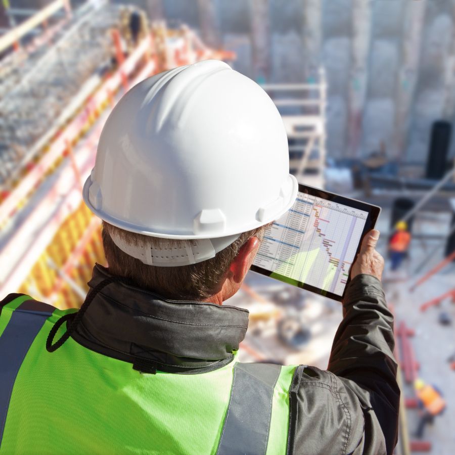 Network Computer Pros Crucial Role Of It In Construction Construction worker looking down at tablet at the top of a building analyzing Cybersecurity for Construction